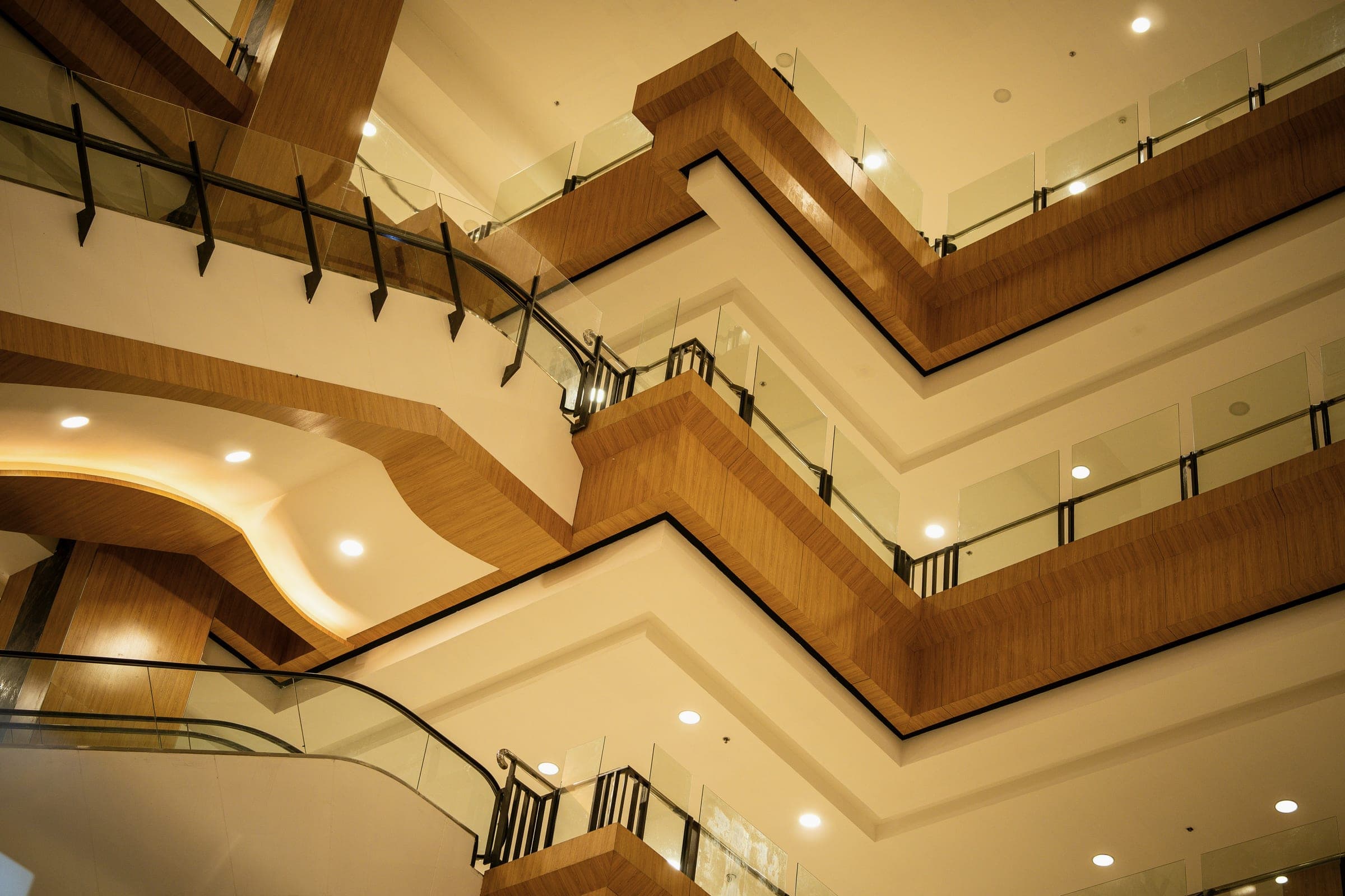 Looking up through a shopping mall atrium at layered wood-clad balconies, glass railings and an escalator.