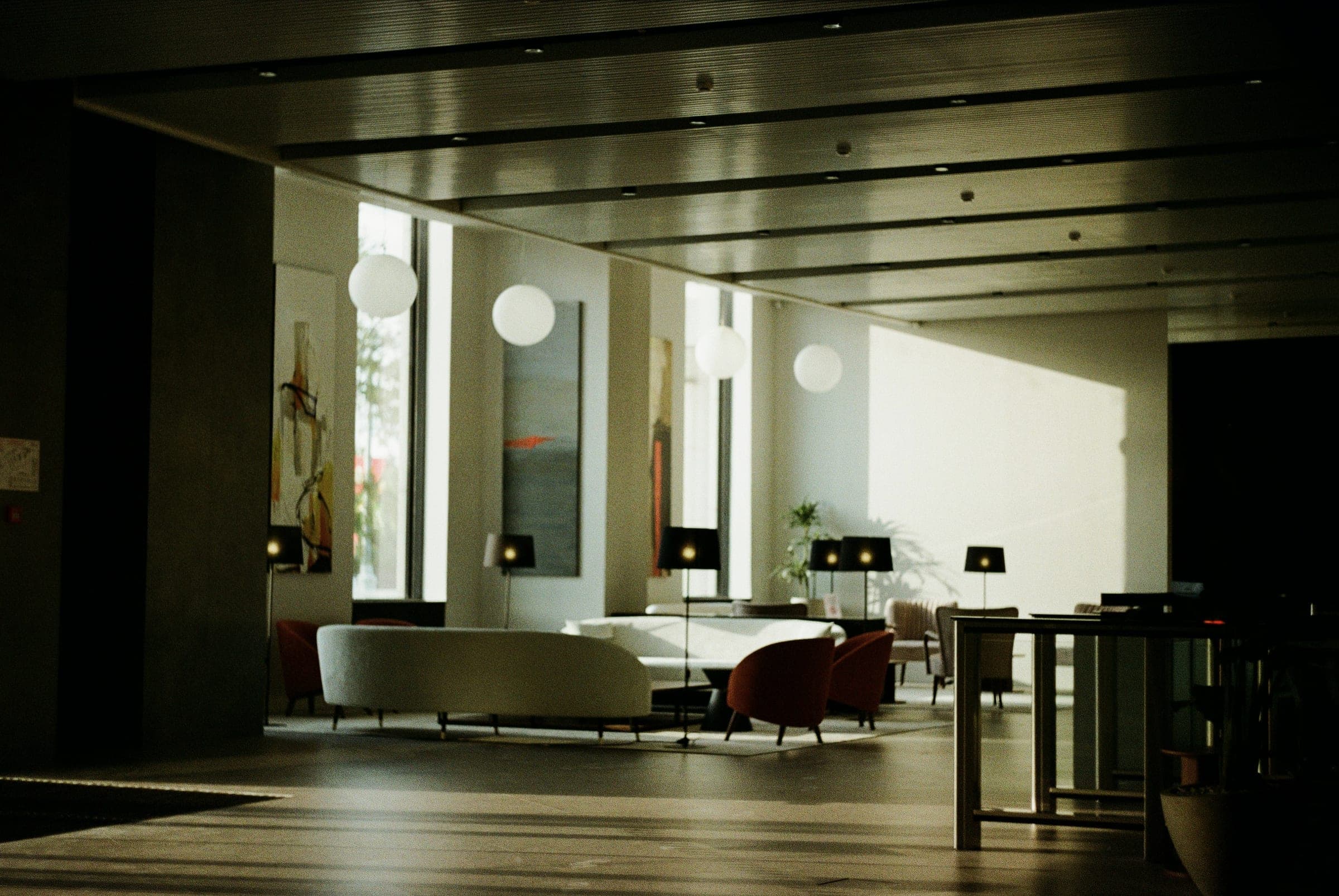 A modern hotel lobby with a curved white sofa, globe pendant lights and warm sunlight on the wall.