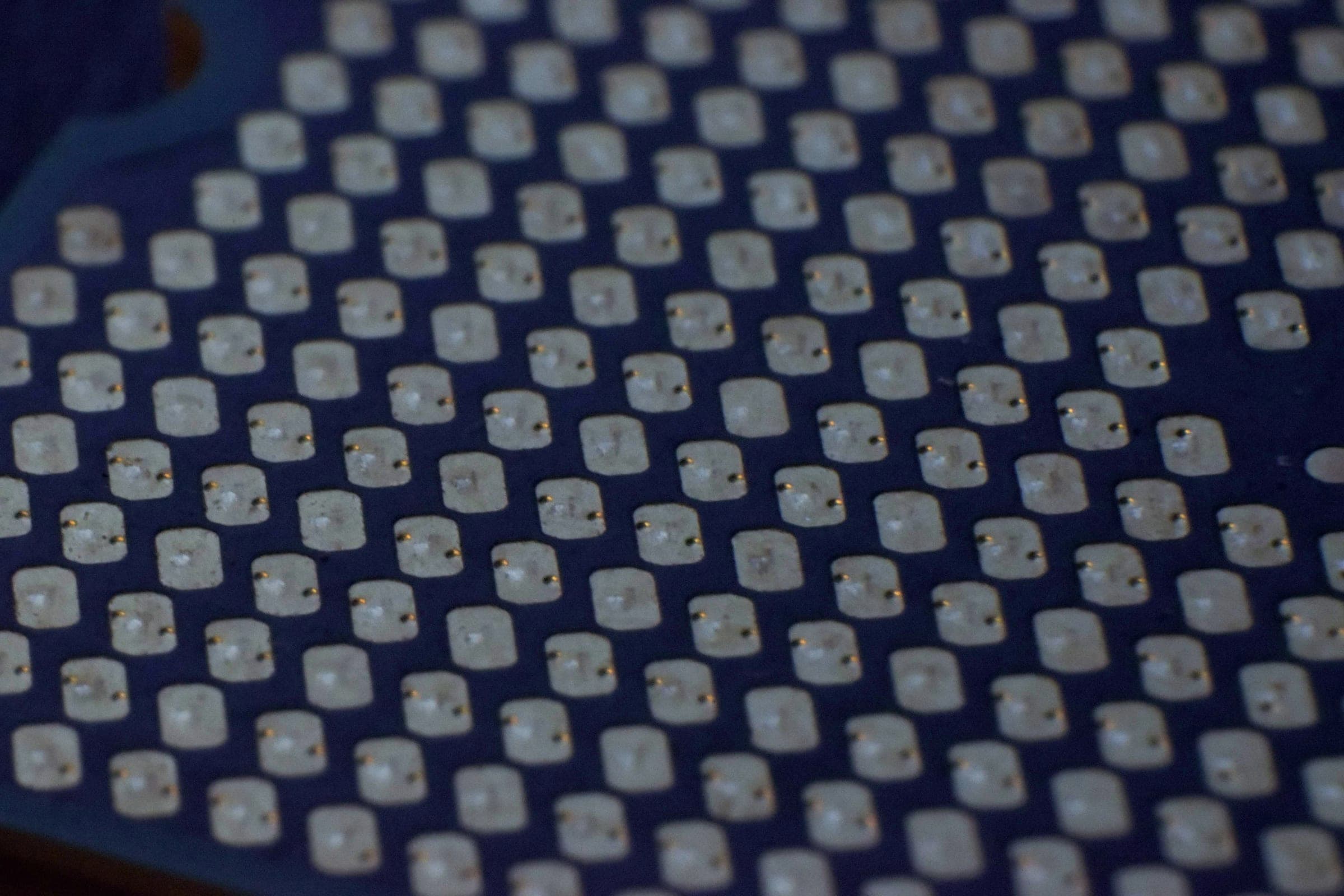 A close-up of an array of solder pads on a blue printed circuit board.