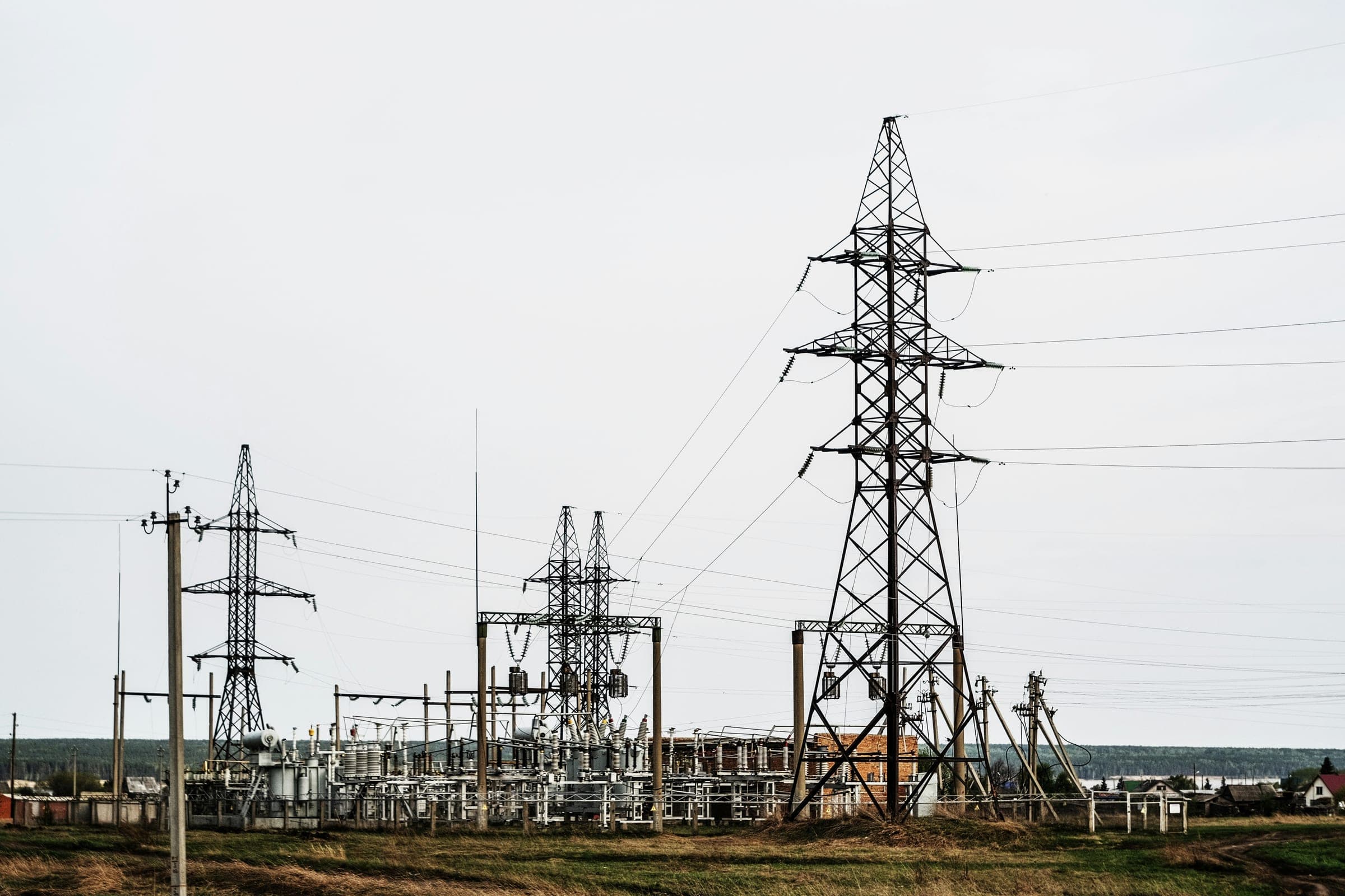 A high-voltage pylon and an electrical substation with transformers across an open field.