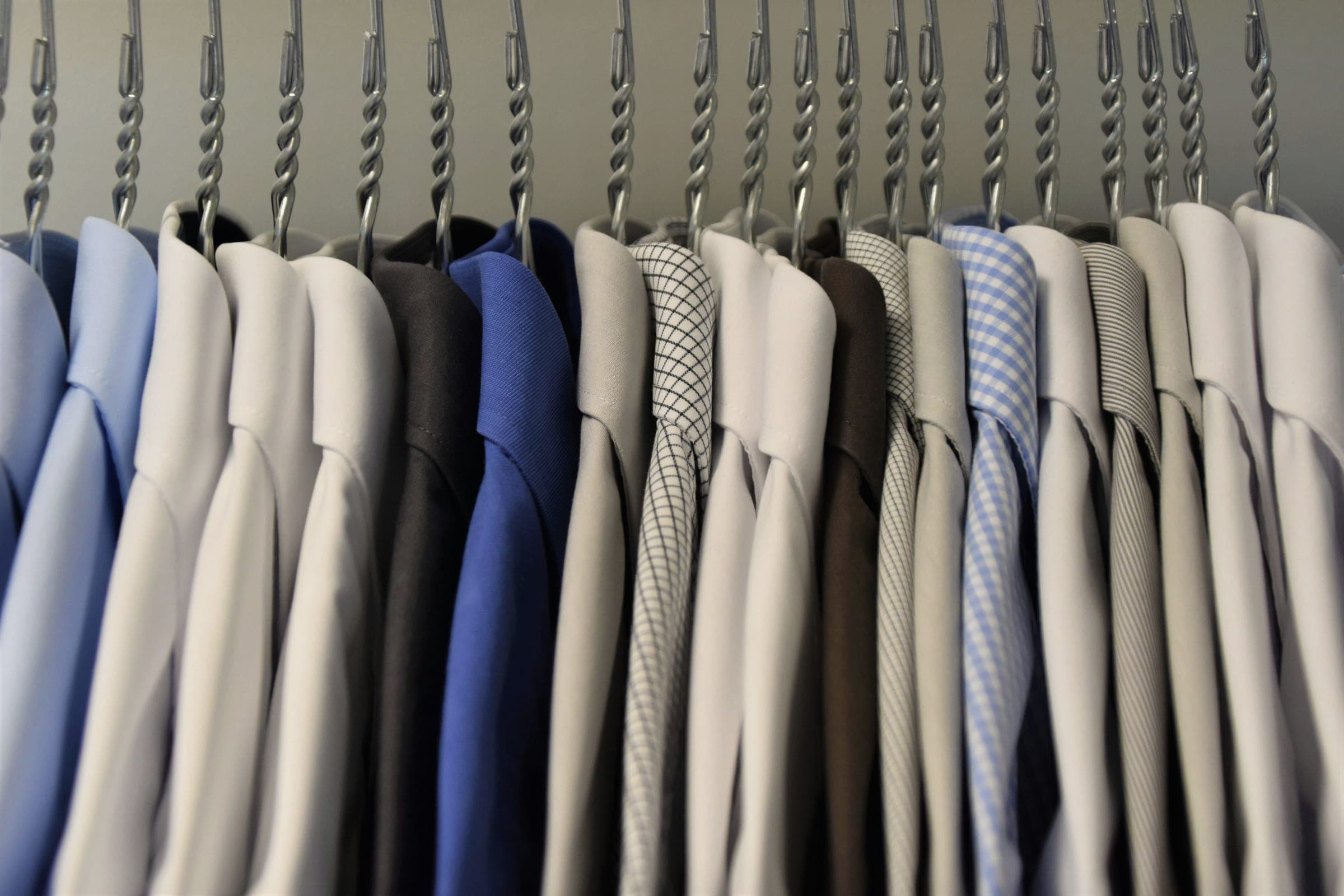 A row of collared shirts in blue, white, gray and checked fabrics hanging from metal hangers.