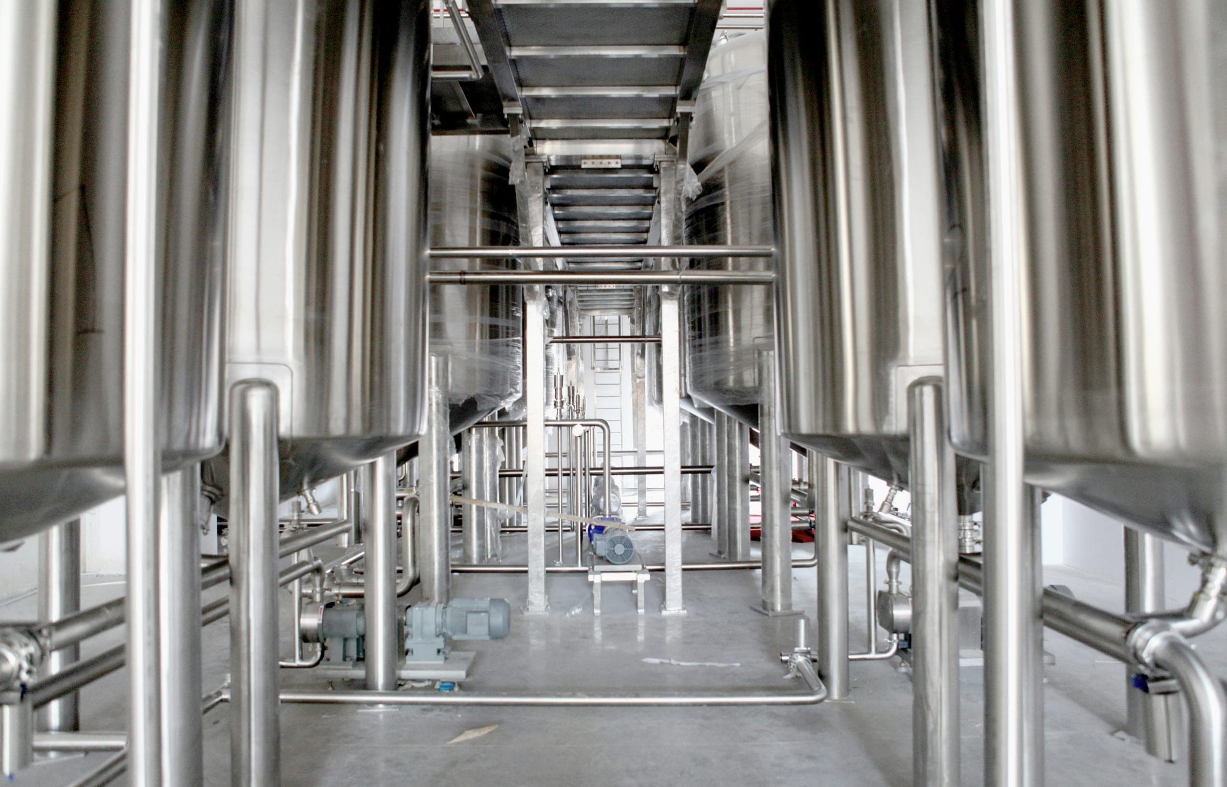 Rows of polished stainless steel tanks and pipework in a brewery or food processing hall.