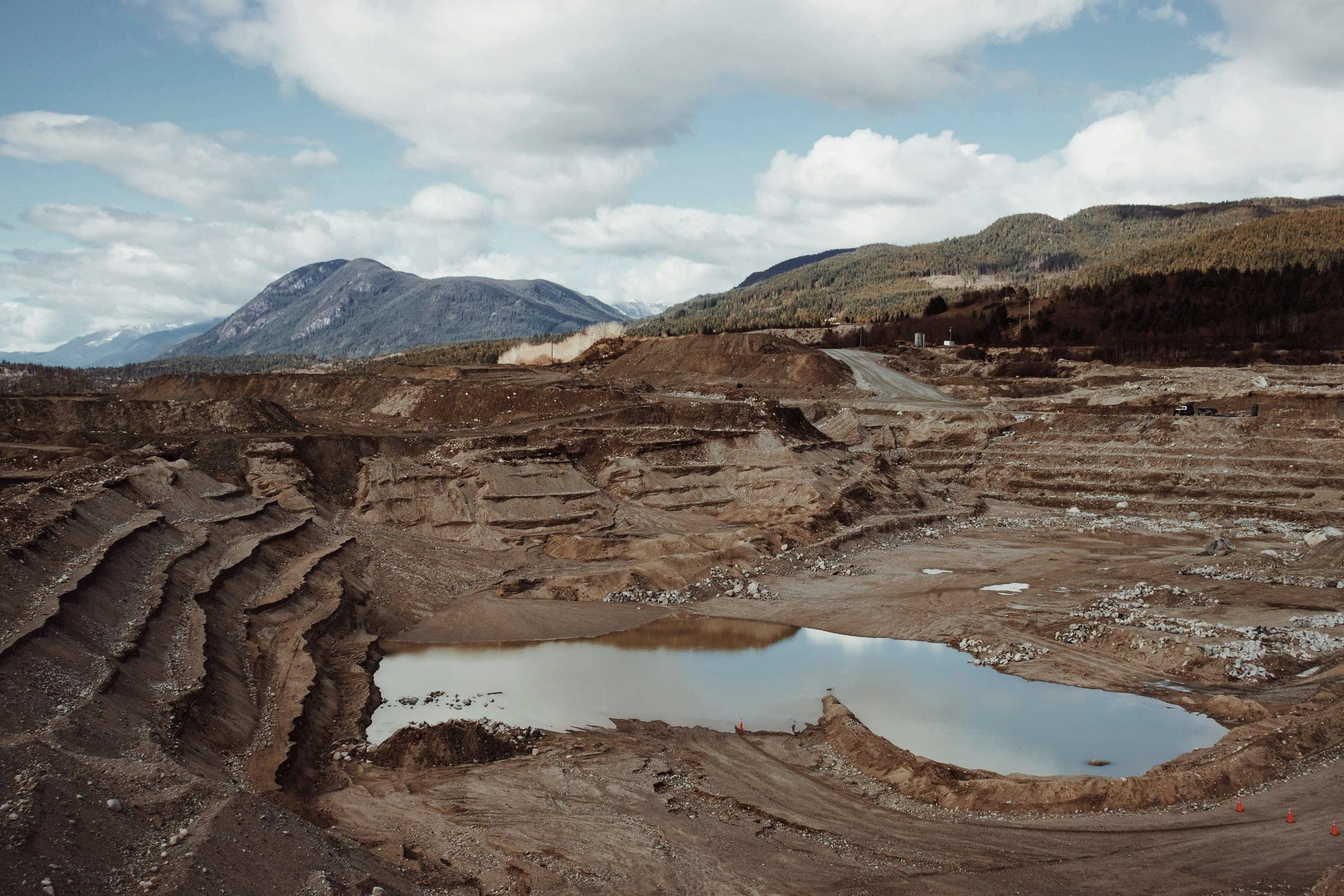A terraced open-pit mine with a pool of water and forested mountains behind.