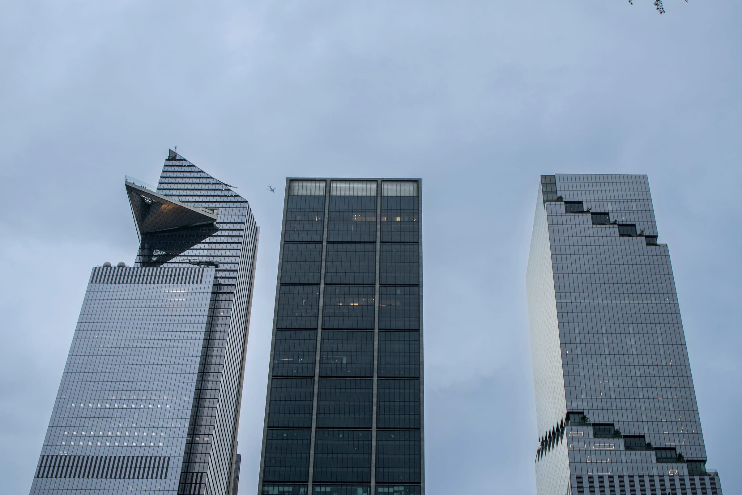 Three glass office towers seen from street level against a gray evening sky.