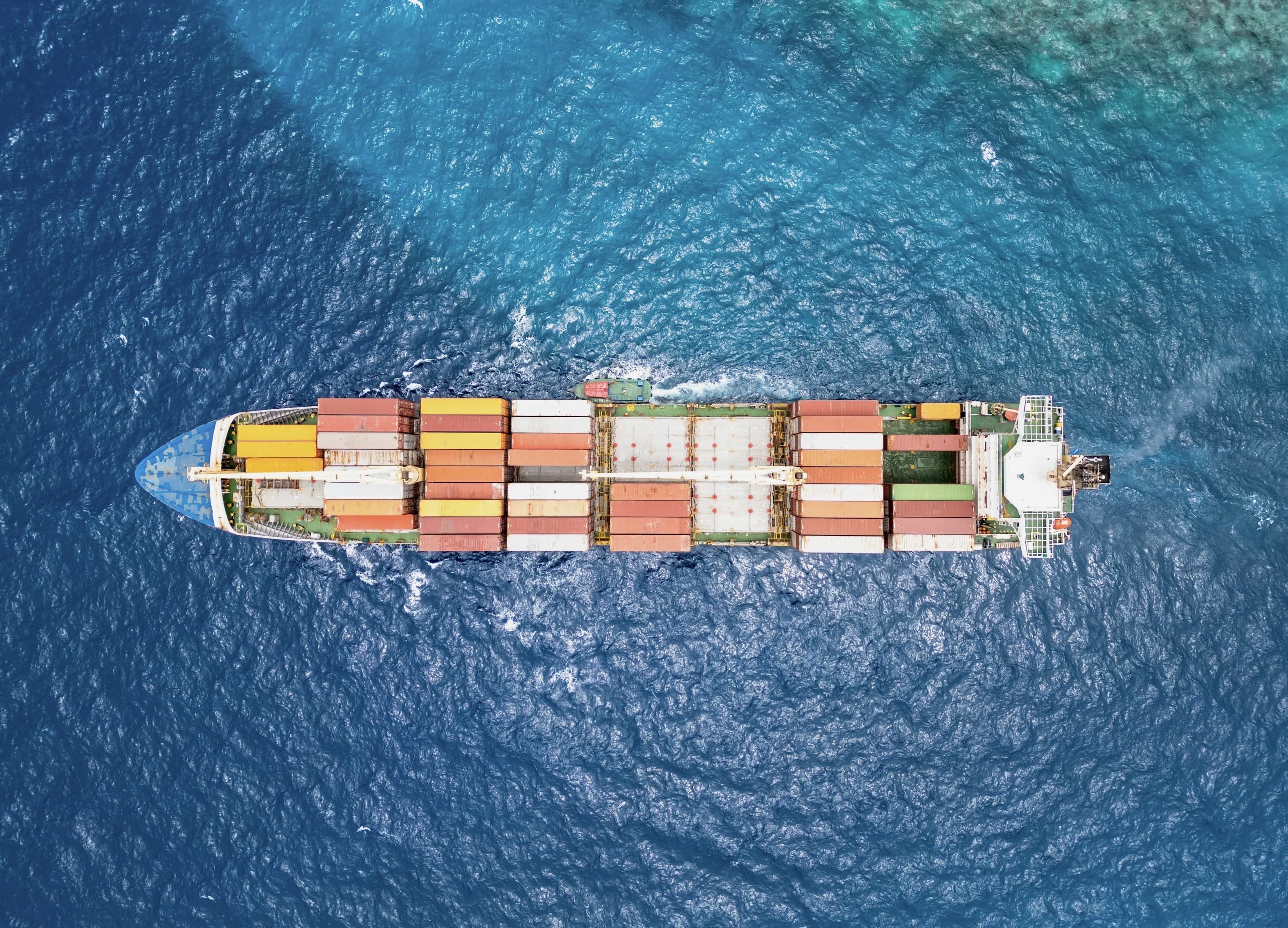 A container ship crossing deep blue ocean, seen from directly above