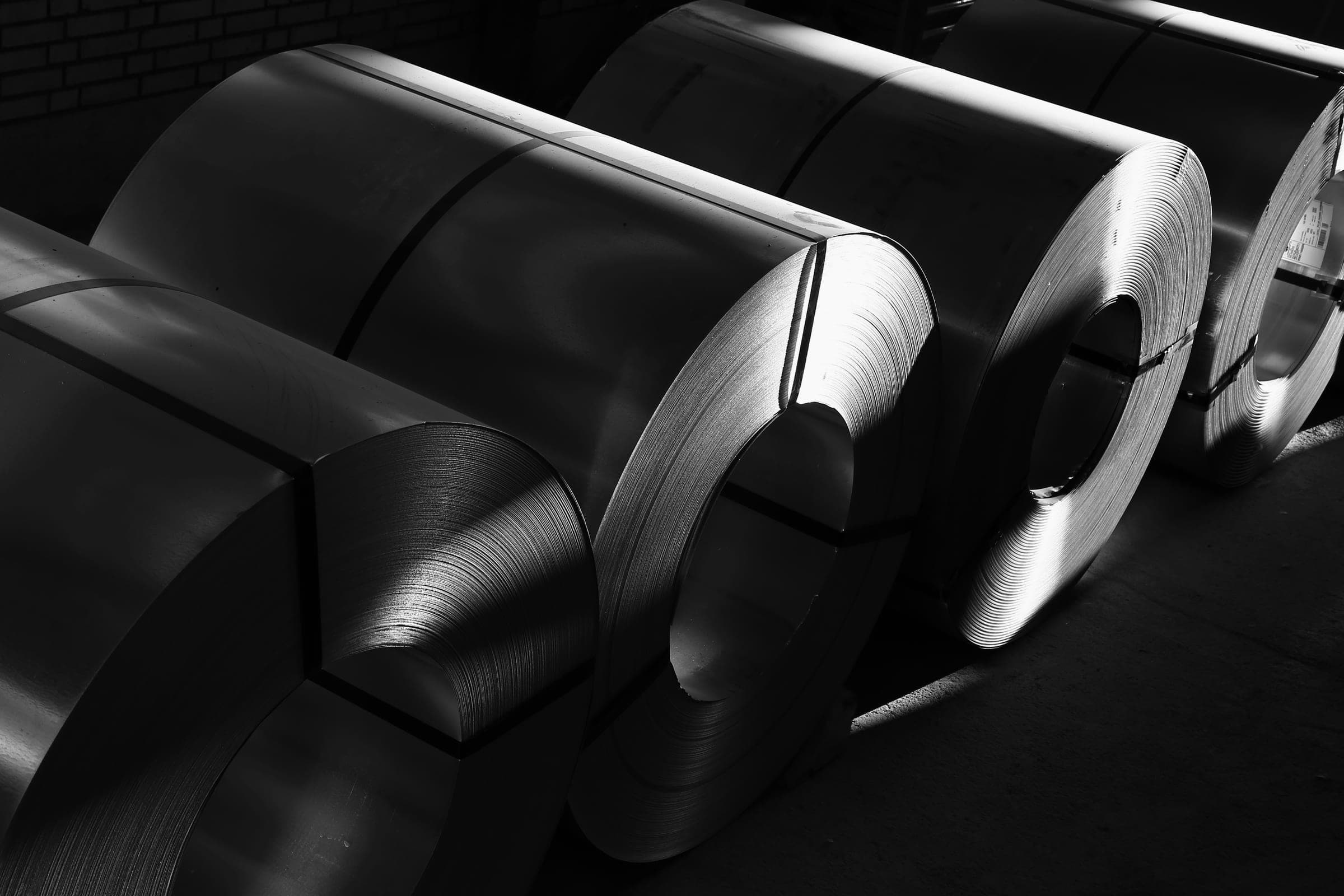 Black and white view of large steel coils lying in a row in raking light.