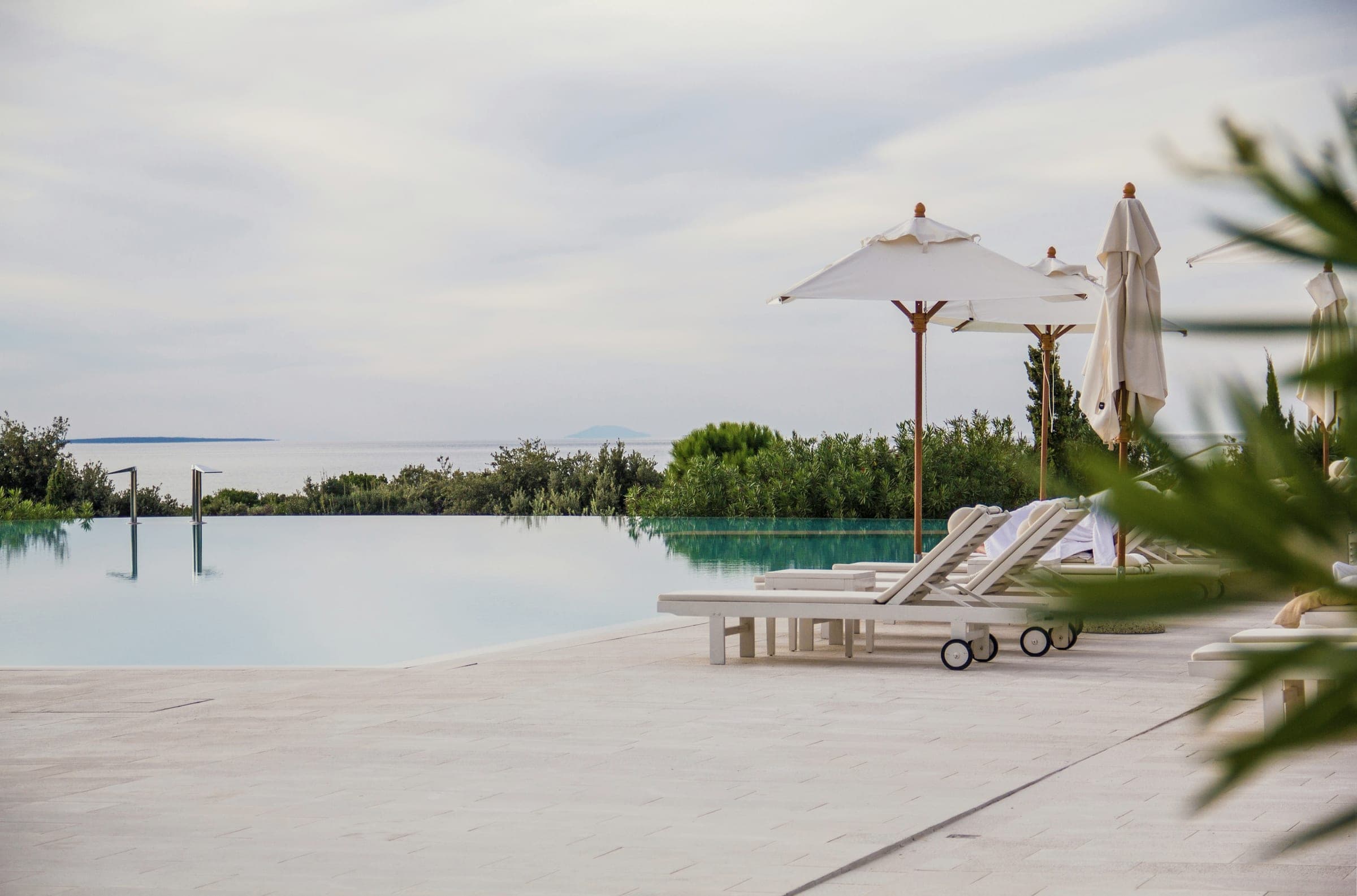 A hotel infinity pool and white loungers and parasols facing the sea.